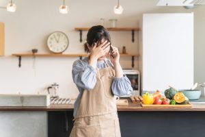 自宅で通話しながらショックをうけたように顔を覆う女性の画像